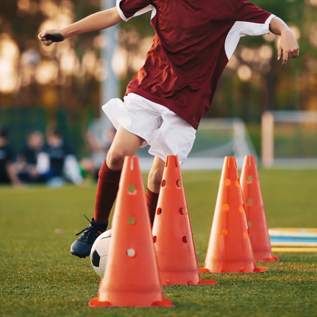 Young soccer player dribbling around cones